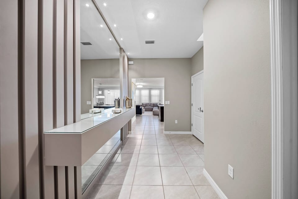 Enter a bright, airy hallway with glossy tile floors and soft beige walls that create a warm welcome. A sleek countertop on the left adds a modern touch, while natural light floods in, enhancing the inviting atmosphere.