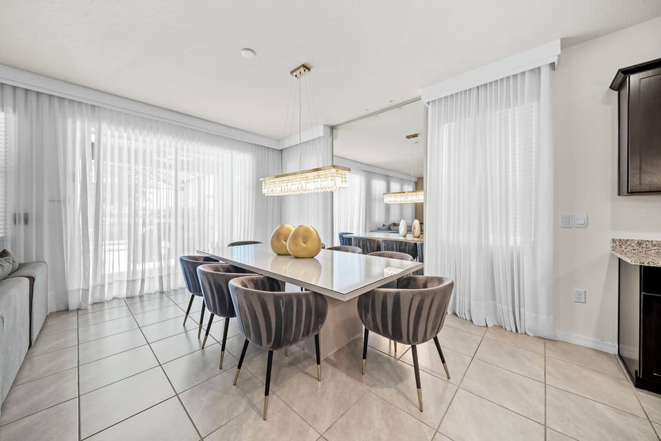 Experience the bright dining area with its sleek marble table and plush chairs, perfect for relaxed meals and conversations. Large windows with sheer curtains fill the space with natural light, creating a warm, welcoming ambiance.