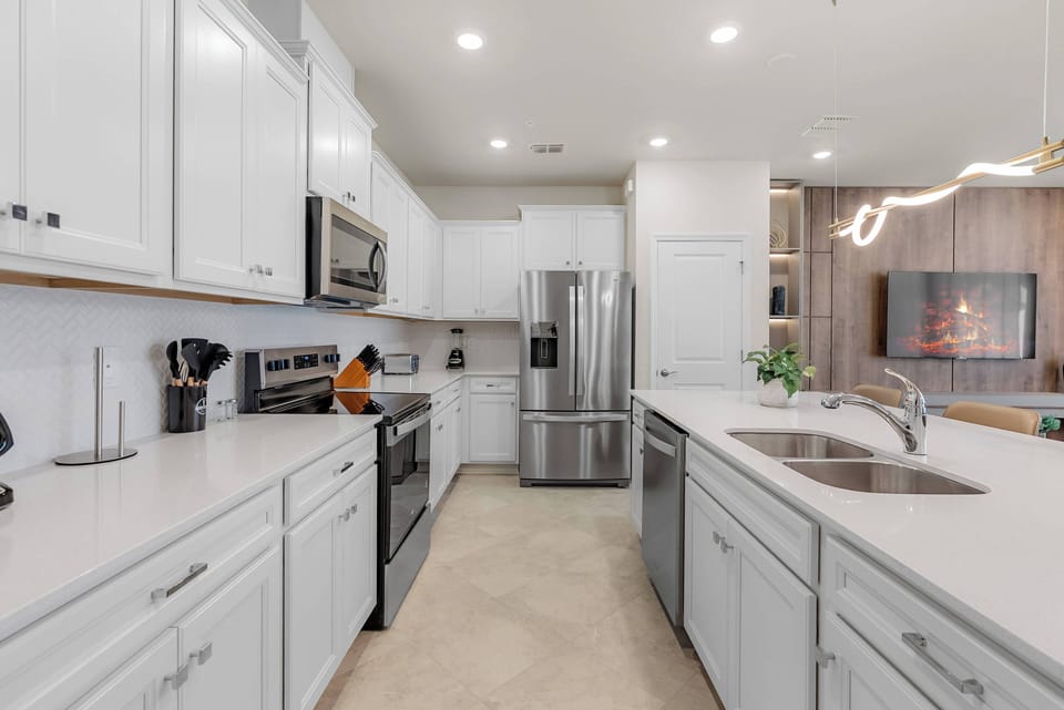 Experience the inviting kitchen with sleek white cabinetry and modern stainless steel appliances, ideal for meal prep. The spacious layout and warm lighting create a delightful cooking atmosphere for all.