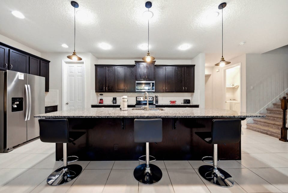 Enjoy culinary adventures in this sleek kitchen with a spacious island and stylish bar stools. The modern cabinetry and warm pendant lighting make it the perfect spot for memorable gatherings and inviting moments.