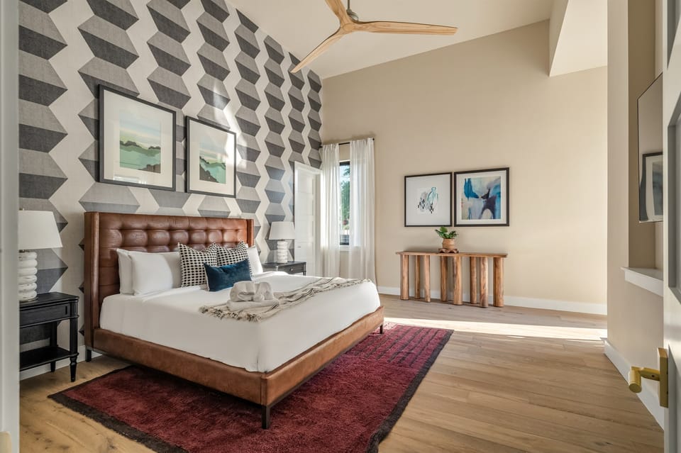 Spacious and elegant primary bedroom featuring a plush king bed, designer accent wall, and modern décor for a relaxing luxury Austin stay.