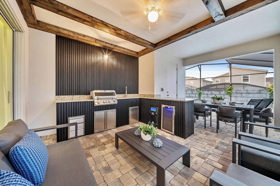 Enjoy a stylish outdoor space featuring a sleek barbecue station and cozy seating, ideal for gatherings. With rich wood beams above and modern stone tiles below, this area blends warmth and sophistication for your enjoyment.