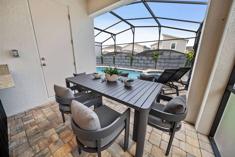Step outside to your private patio, where a stylish table set invites al fresco dining against a backdrop of glistening pool water. The sleek, modern chairs and paver stones add to the inviting atmosphere, perfect for relaxation.