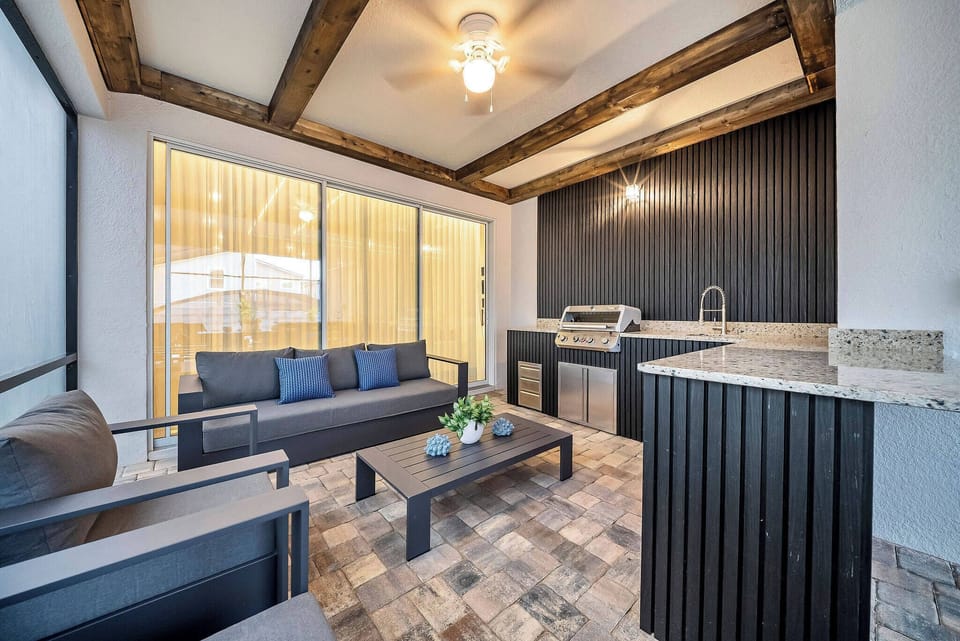 Unwind in our stylish outdoor lounge featuring rich wood beams and a sleek black accent wall, with comfy seating, a built-in grill, and elegant stone countertops, making it perfect for casual gatherings and al fresco dining.