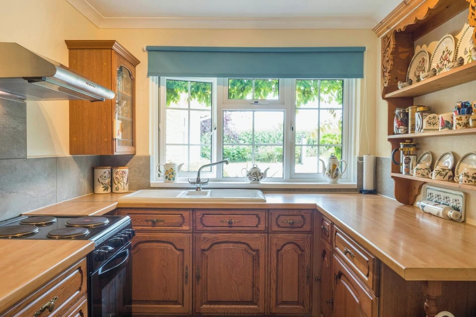 Wooden kitchen cabinets and worktops around a sink beneath a window with a blue blind