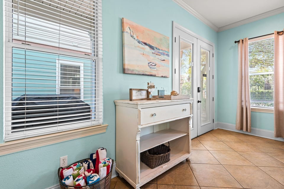A bright, coastal-inspired entry with seafoam blue walls and a white console table. Large windows fill the space with natural light.