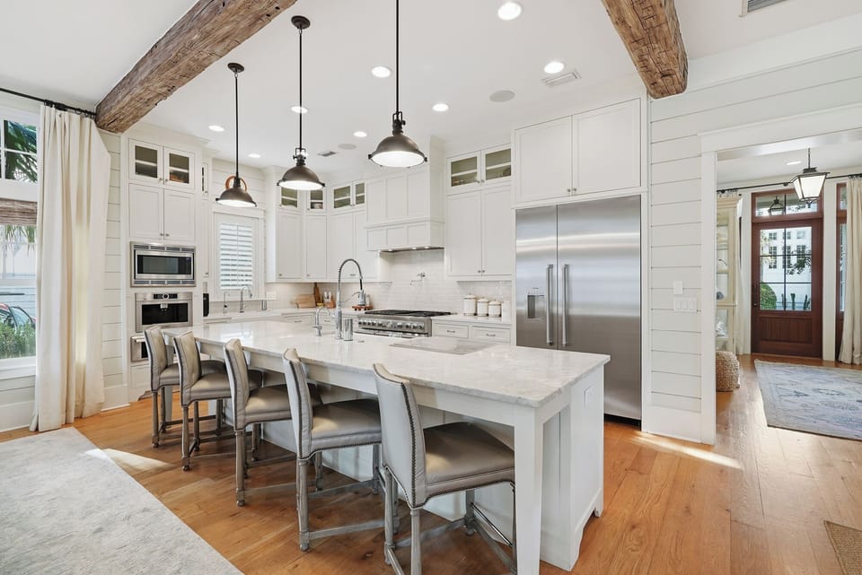A stunning gourmet kitchen awaits you, featuring vaulted ceilings with rustic beams, sleek white cabinetry, marble countertops, and a spacious island perfect for gathering with family and friends.