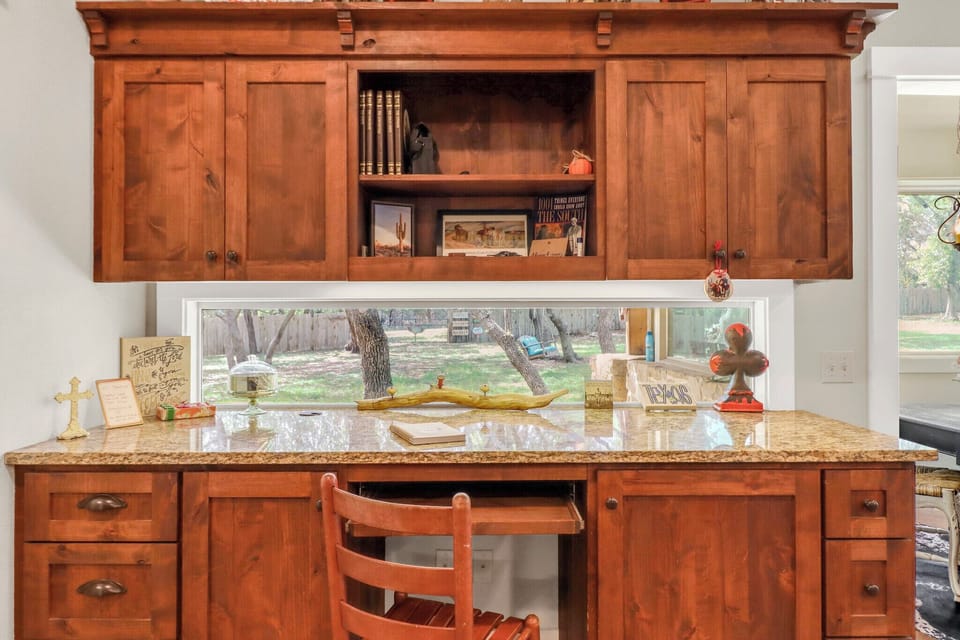 Your workspace awaits with warm wood cabinetry, granite countertop, and peaceful garden views through the window above.