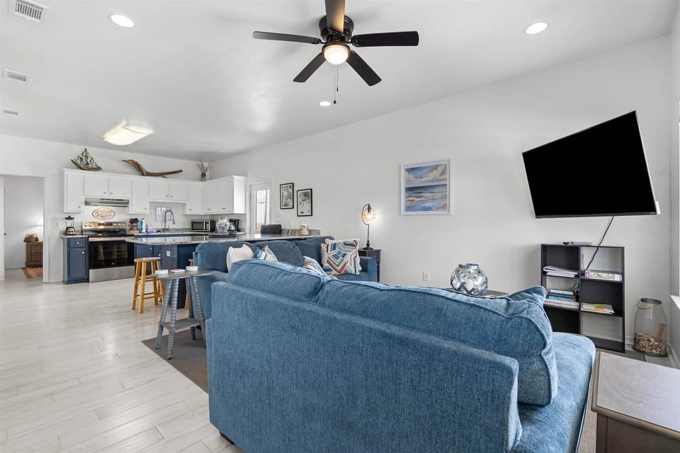 Relax in your spacious open-concept living space with plush blue seating, modern kitchen, and entertainment center for perfect vacation comfort.