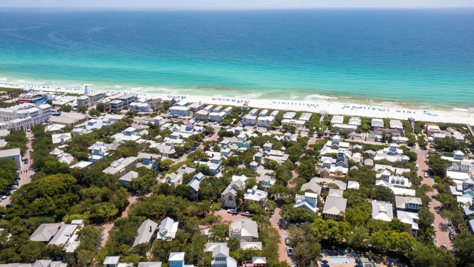 Aerial view of a charming beachfront community nestled among lush greenery, with pristine white sand and turquoise waters just steps away.