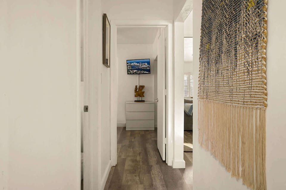 The hallway connecting the two bedrooms — with a statement macramé wall piece and the living room TV visible at the far end. Every detail in this home was chosen with care