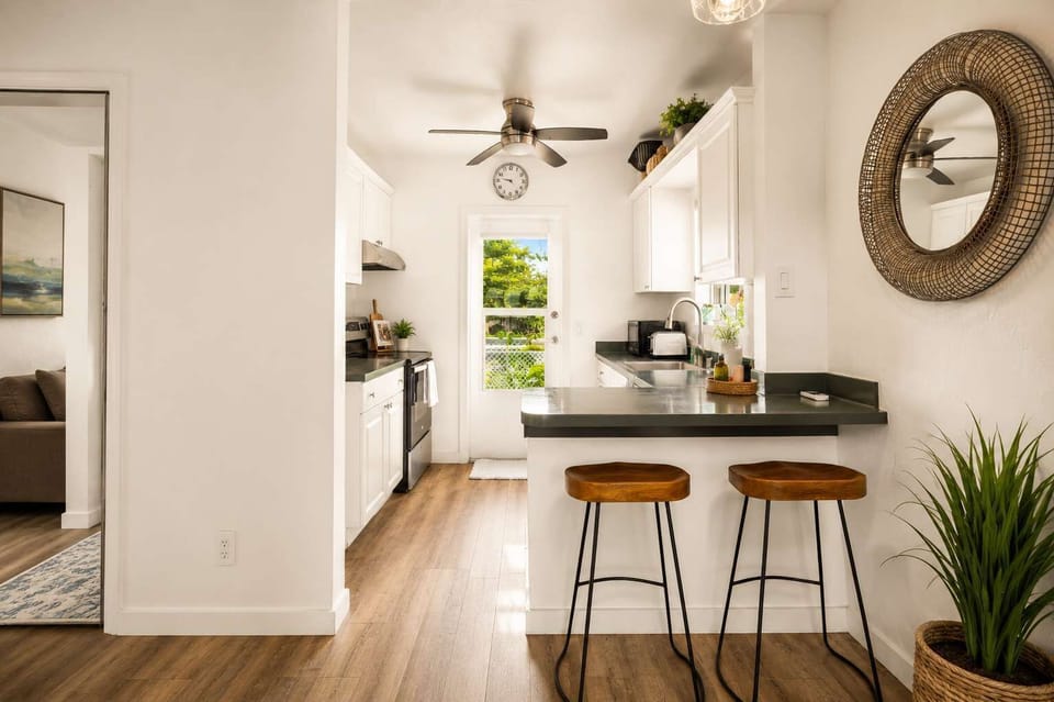 Open-plan layout connecting living room to kitchen  bar seating, ceiling fan, and coastal details that make the whole space feel airy, easy, and relaxed