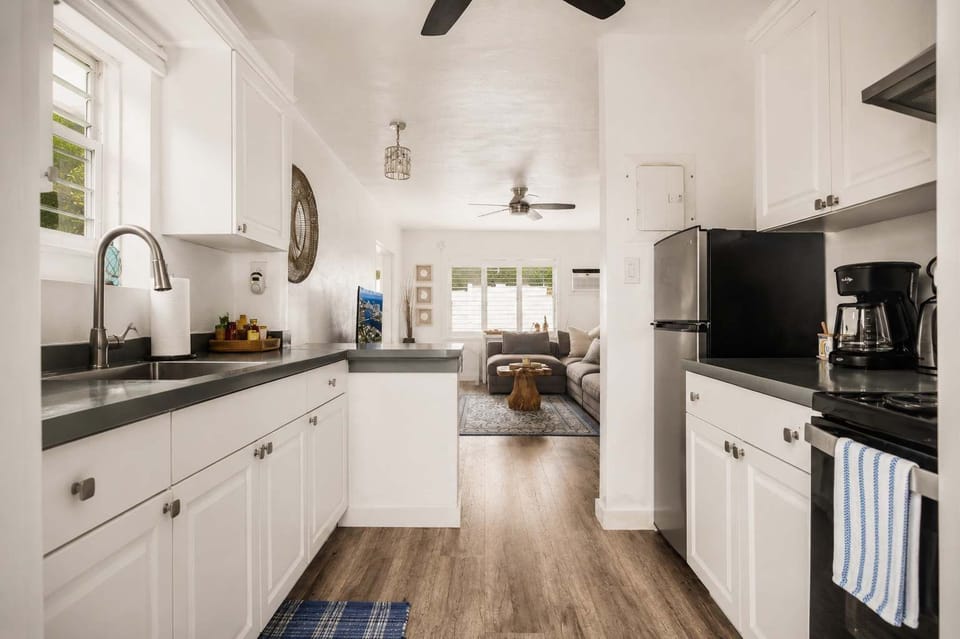 Fully equipped kitchen with white cabinetry, dark countertops, stainless steel appliances, and a view straight through to the living room — everything you need for a real home-cooked meal