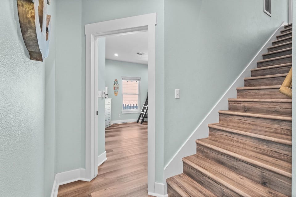 Interior stairway and hallway with modern flooring and coastal paint tones leading to spacious bedrooms and shared living areas.