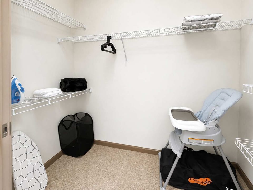 Walk-in closet with open shelving, hanging space, and handy extras including an iron, ironing board, and high chair.