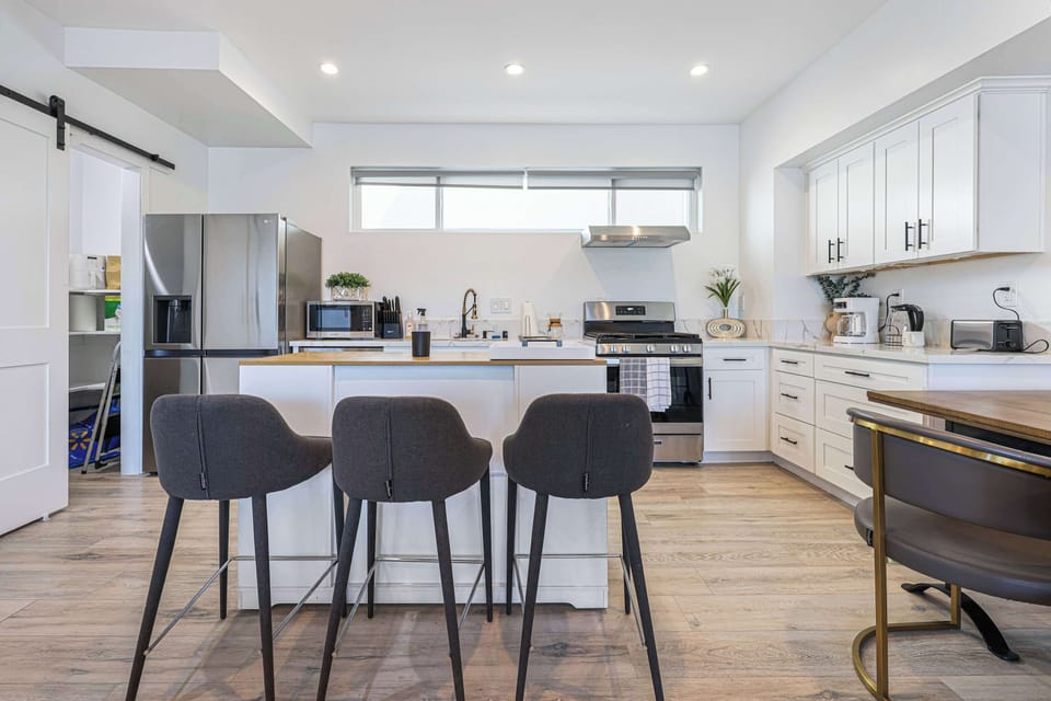 This bright, open kitchen has white cabinets, stainless steel appliances, and an island with seating for three. A hidden walk-in pantry behind a barn door keeps everything neat.
