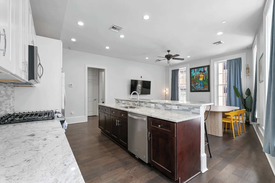 Bright open kitchen with a large island, quartz counters, gas range, stainless appliances, and deep sink. Fully stocked with cookware, dishes, coffee maker, toaster, pantry basics, and a cozy dining nook.