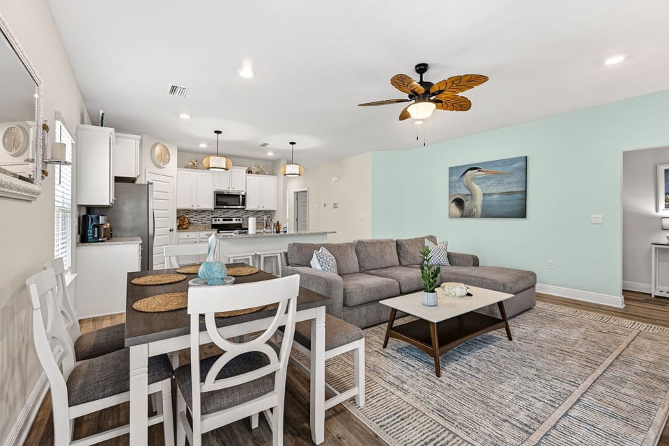 Bright coastal-style open living space with kitchen, dining, and large sectional