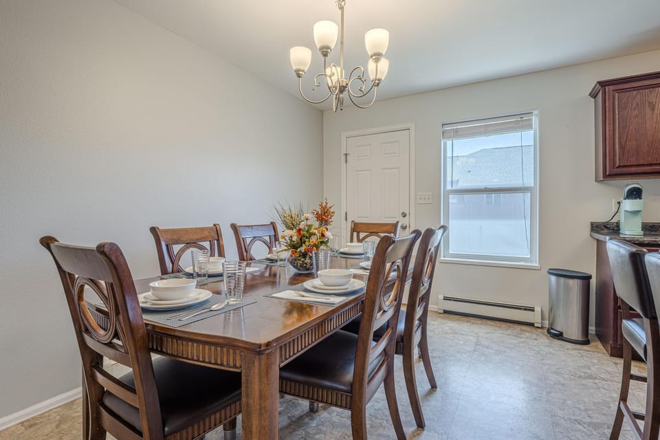 Dining area with a dark wood table set for six, floral centerpiece, beige tile floor, and soft overhead chandelier lighting.