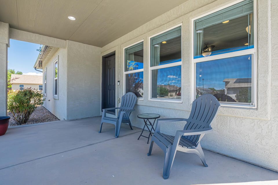 Two gray Adirondack chairs flank a small round glass-top table on the covered concrete porch.