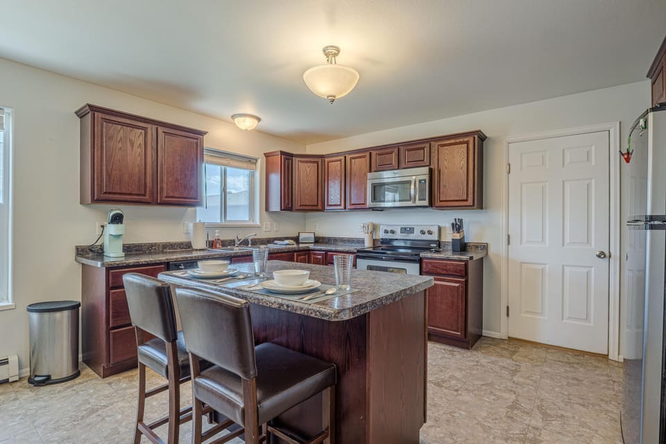 Kitchen with dark wood cabinets, stainless steel appliances, a granite-patterned island, and two brown leather bar stools.