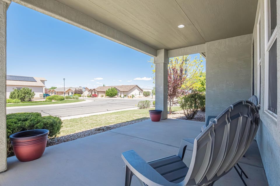 Shaded concrete porch with two gray Adirondack chairs and red ceramic planters overlooking the street.