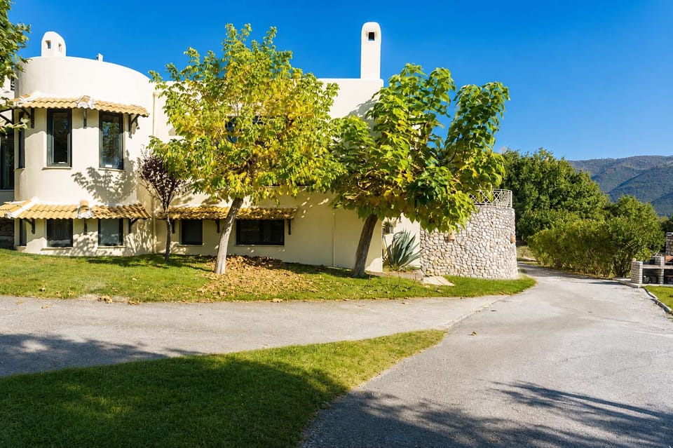 The property blends naturally into the surrounding landscape, framed by olive trees, forest scenery, and wide open lawns