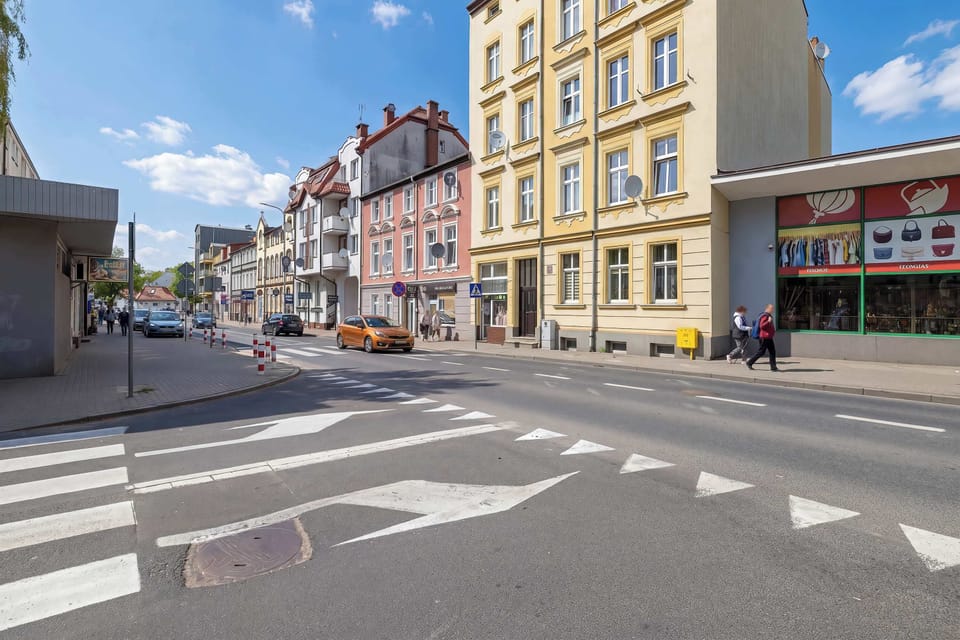 A lively urban streetscape lined with colorful historic buildings and pedestrian crossings. Bright blue skies enhance the vibrant city atmosphere.