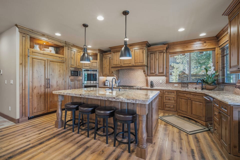 Your gourmet kitchen features warm wood cabinetry, granite countertops, a spacious island with seating, and modern appliances—perfect for preparing delicious meals while enjoying natural light streaming through the window.