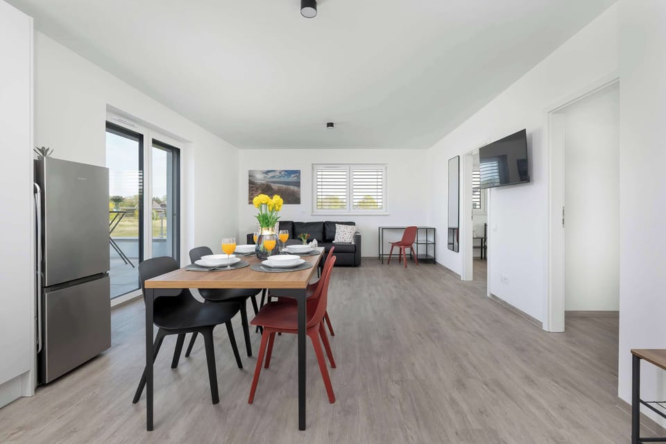 A modern kitchenette and dining area with wooden floors and bright white walls. The open-plan layout feels spacious and clean.