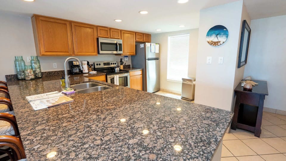 Warm, modern kitchen featuring granite countertops, stainless‑steel appliances and inviting bar seating perfect for casual dining or gathering. Thoughtful lighting and clean design create a welcoming space for cooking, hosting and relaxing together.