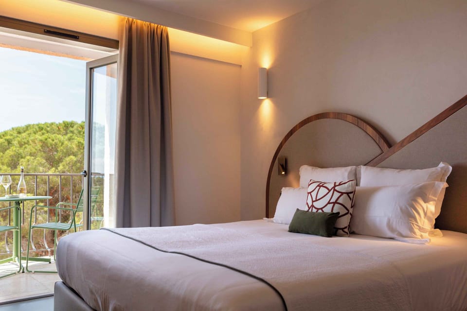 King bed with wooden headboard and white linens — greenery from the park balcony visible behind