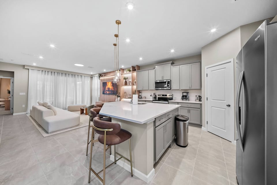 Enjoy a beautifully designed kitchen with sleek gray cabinetry and white countertops, opening into a cozy, light-filled living area, ideal for casual meals or relaxing with loved ones.
