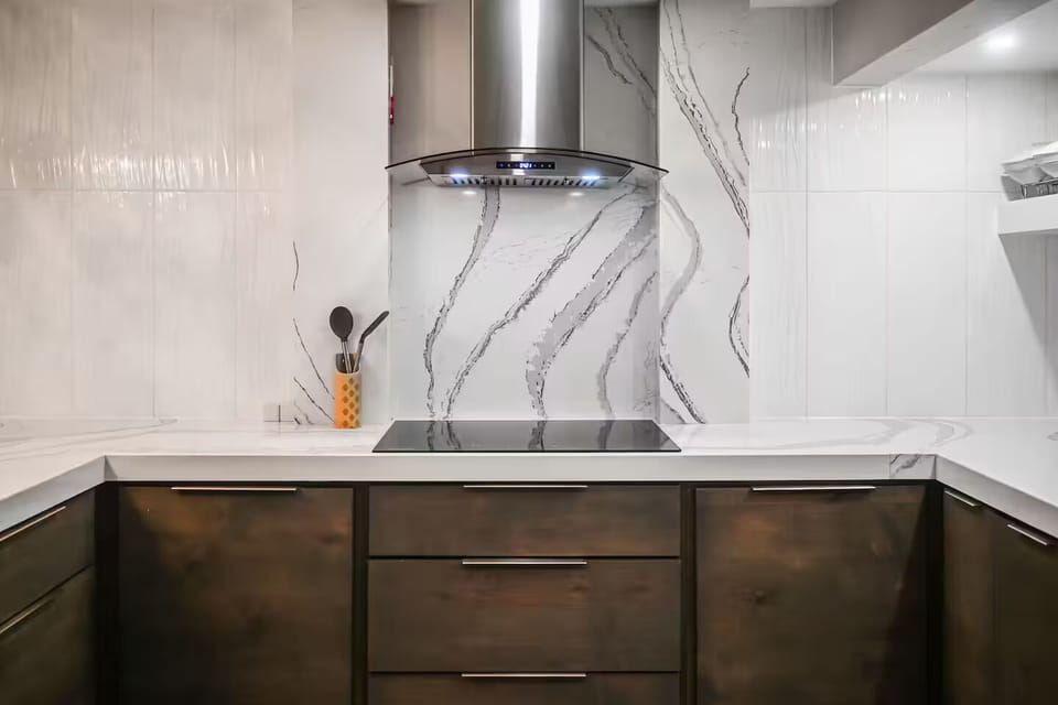 Sleek cooktop with modern range hood and designer stone backsplash.