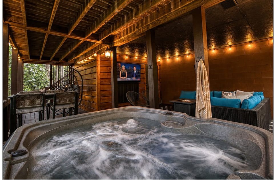Covered deck oasis: hot tub, outdoor TV, bar seating & string lights