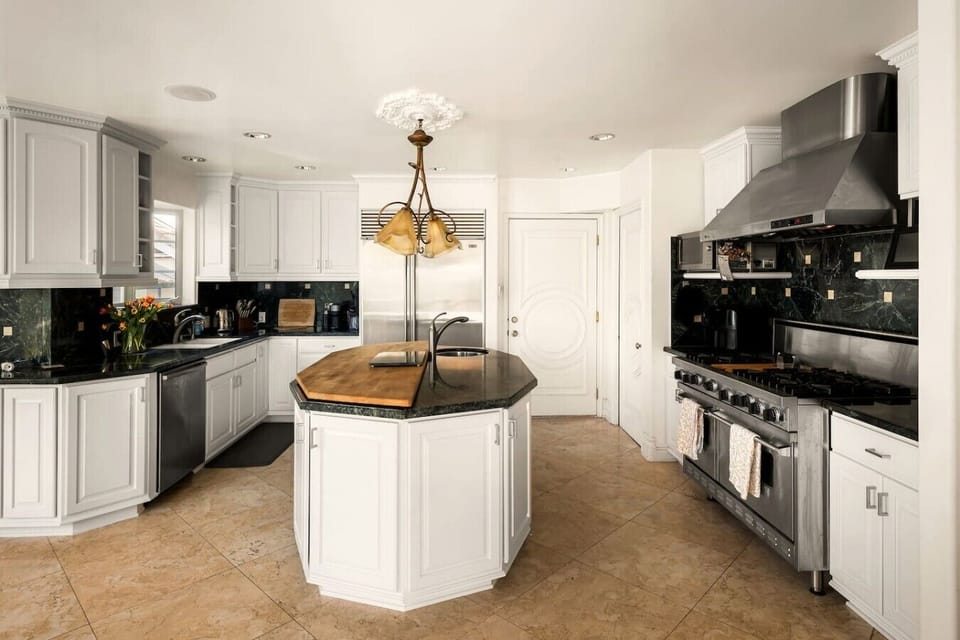 Chef`s kitchen with six-burner gas stove, kitchen island, custom cabinetry, and pendant lighting.