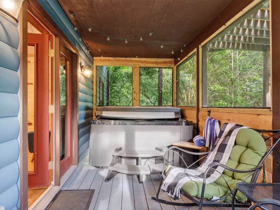 Private screened porch with a hot tub and lounge seating tucked into the trees.