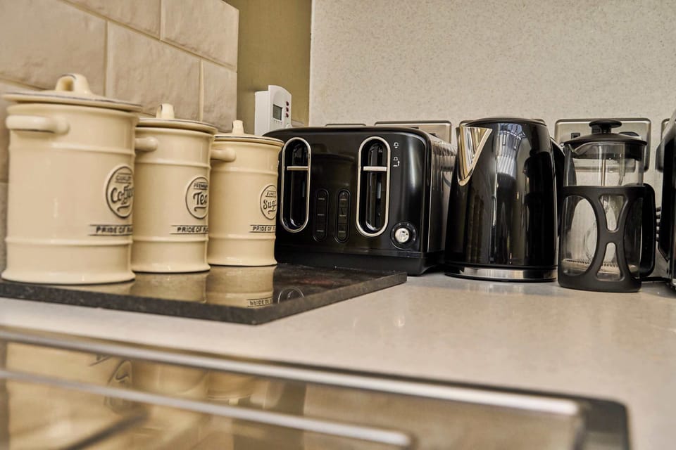 A well-equipped breakfast station featuring matching black appliances, including a toaster, kettle, French press coffee maker, and ceramic storage canisters for guest convenience.