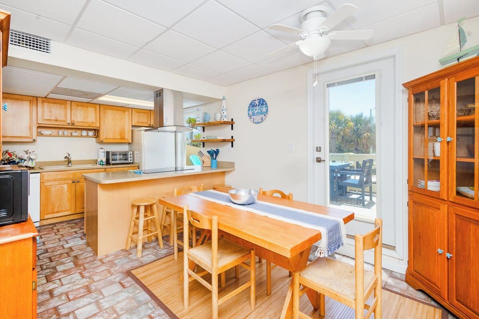Gather around the warm wooden dining table in your fully-equipped kitchen, where morning coffee and home-cooked meals feel extra special with views of swaying palms just beyond the glass door.
