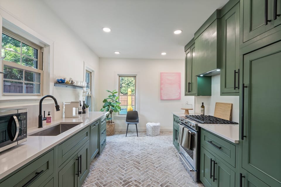 Fully equipped kitchen with sage green cabinetry, herringbone tile floors, gas stove, and stainless appliances. Dishwasher, full cookware, cooking basics, wine glasses, and Keurig coffee maker provided.