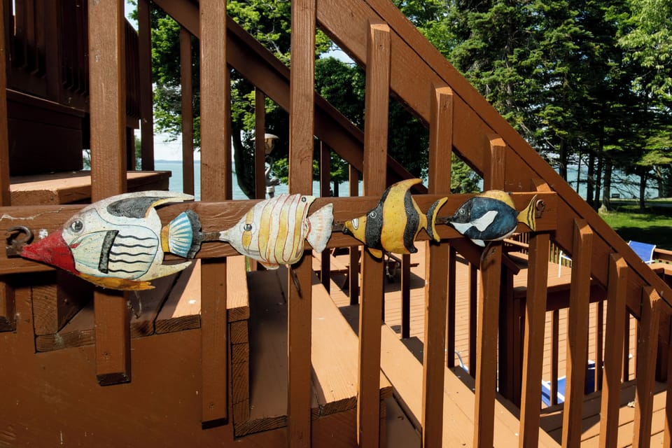 Lakefront deck features charming handcrafted wooden fish decorations, surrounded by lush trees and peaceful water views—a delightful spot for you to unwind outdoors.