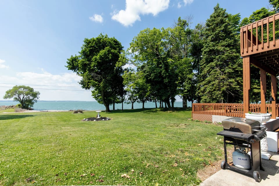 Expansive waterfront property featuring a wooden deck with BBQ facilities, open lawn, and mature trees leading to a serene lakeside setting.