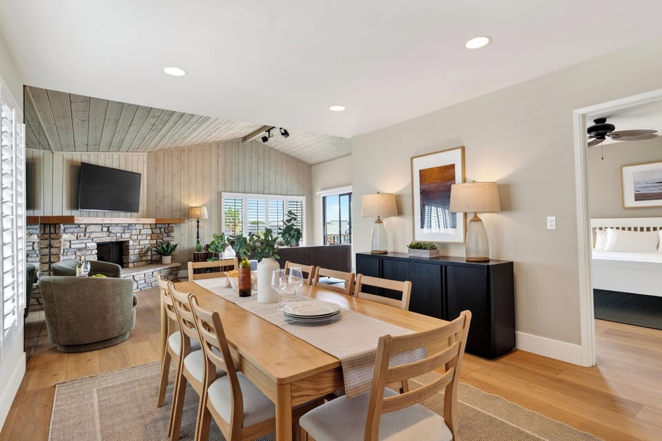 Open dining and lounge area with a stone fireplace, ocean-view balcony access, and relaxed coastal style.