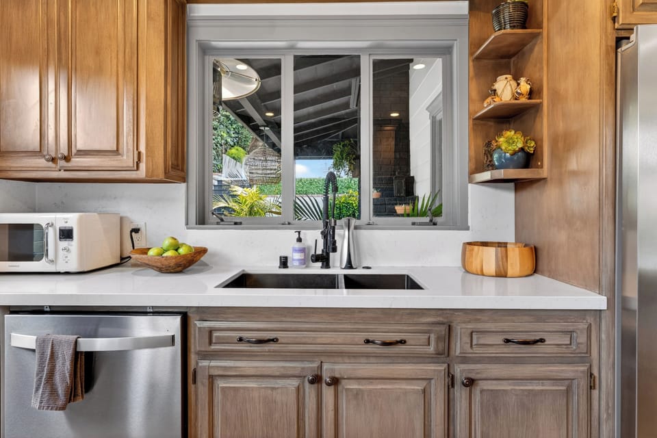 A deep dual-basin under-mount sink framed by a picturesque window looking out onto the lush backyard greenery.