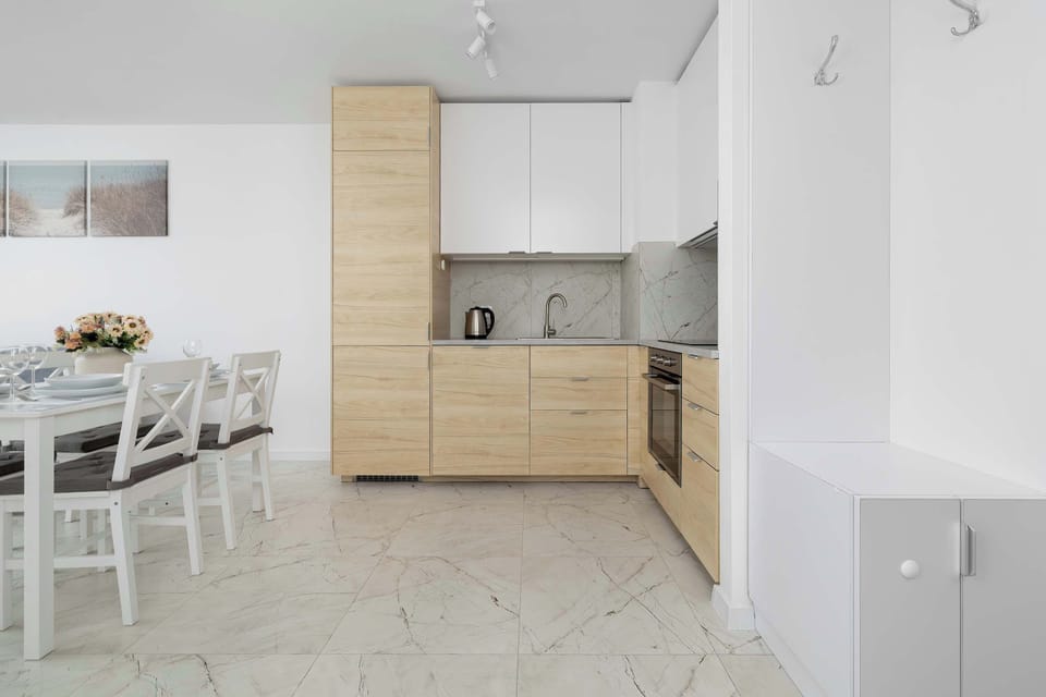 The kitchen and entryway area feature tall, built-in wooden storage cabinets extending to the ceiling. The marble-look flooring creates a continuous, clean aesthetic across the entire floor plan.