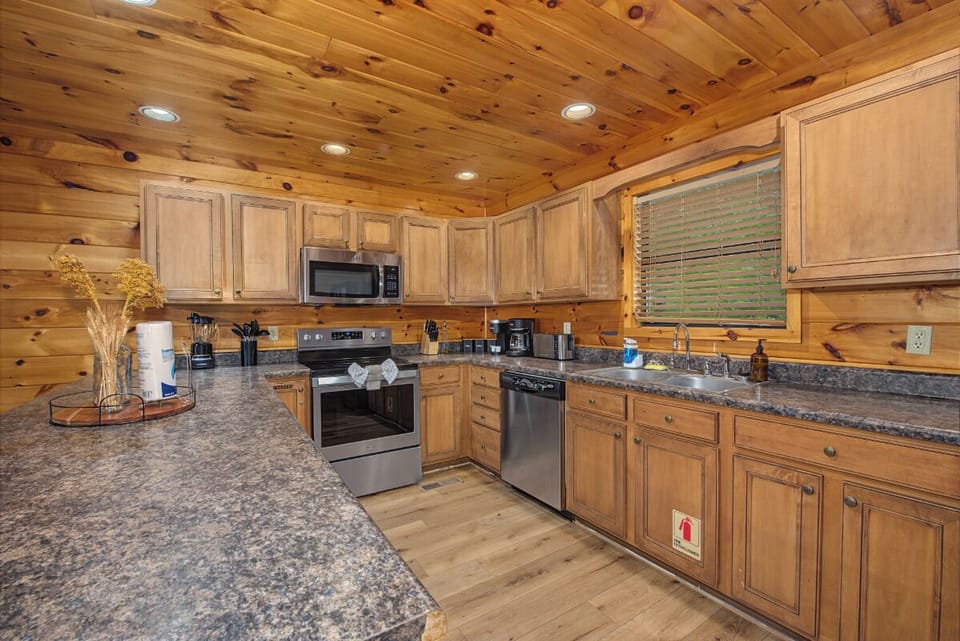Your spacious cabin kitchen features warm knotty pine walls and ceilings, granite countertops, and stainless appliances, creating a cozy yet modern space where you can gather and cook memorable meals together.