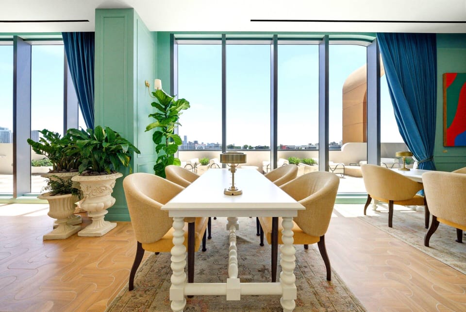 Enjoy the natural light pouring through large windows, brightening the stylish dining area. Soft blue and warm earthy tones enhance the elegant furniture, and lush greenery adds a refreshing touch to your experience.