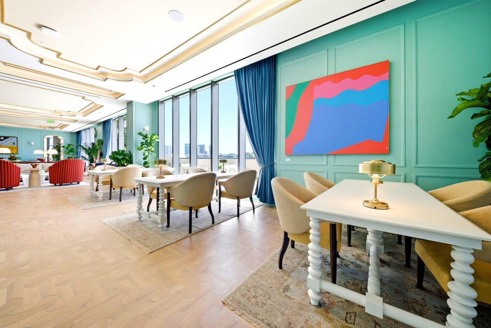 Experience the bright and airy dining area with a striking teal accent wall and vibrant artwork that adds color. Plush seating around elegant tables creates an inviting atmosphere ideal for meals and gatherings.