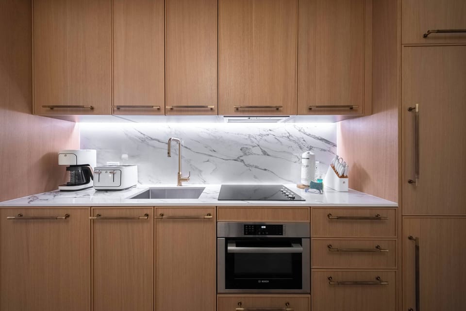 This stylish kitchen boasts warm wooden cabinets and elegant marble countertops that inspire culinary creativity, while soft under-cabinet lighting highlights modern appliances for a functional yet chic atmosphere.