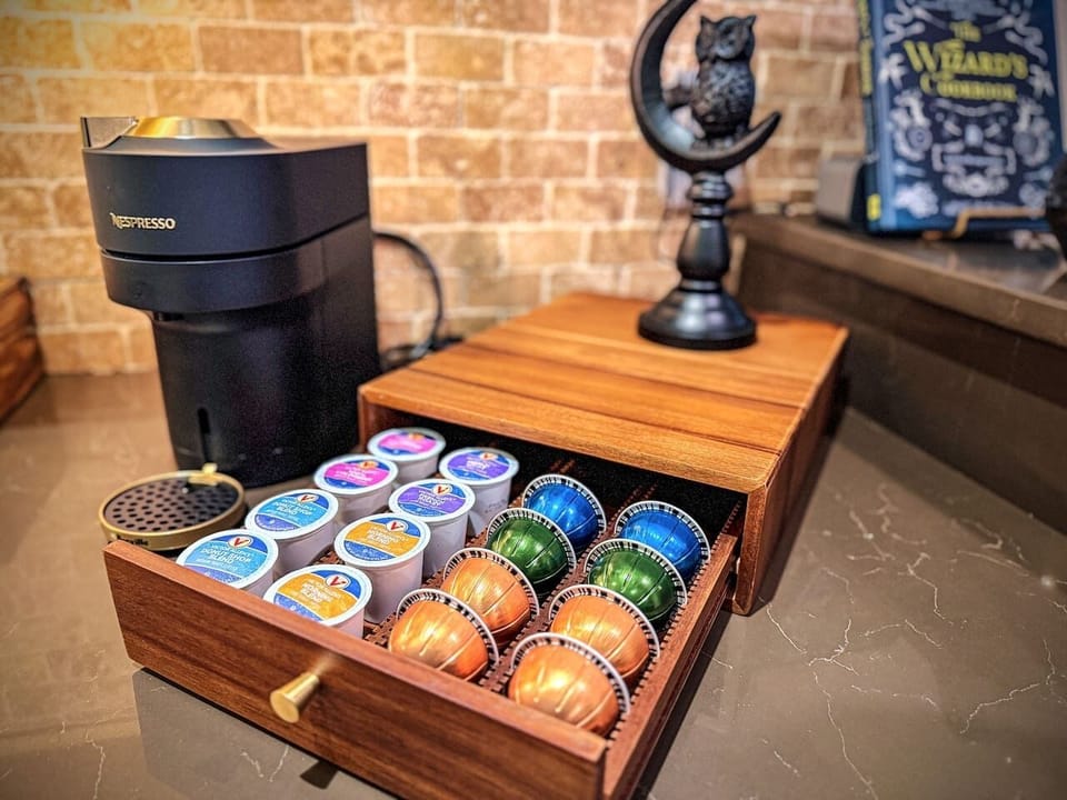 Nespresso Vertuo loaded, walnut drawer stocked with colorful pods, a cauldron-shaped sugar bowl watching over it all. First one up makes the coffee and feels like a wizard doing it.